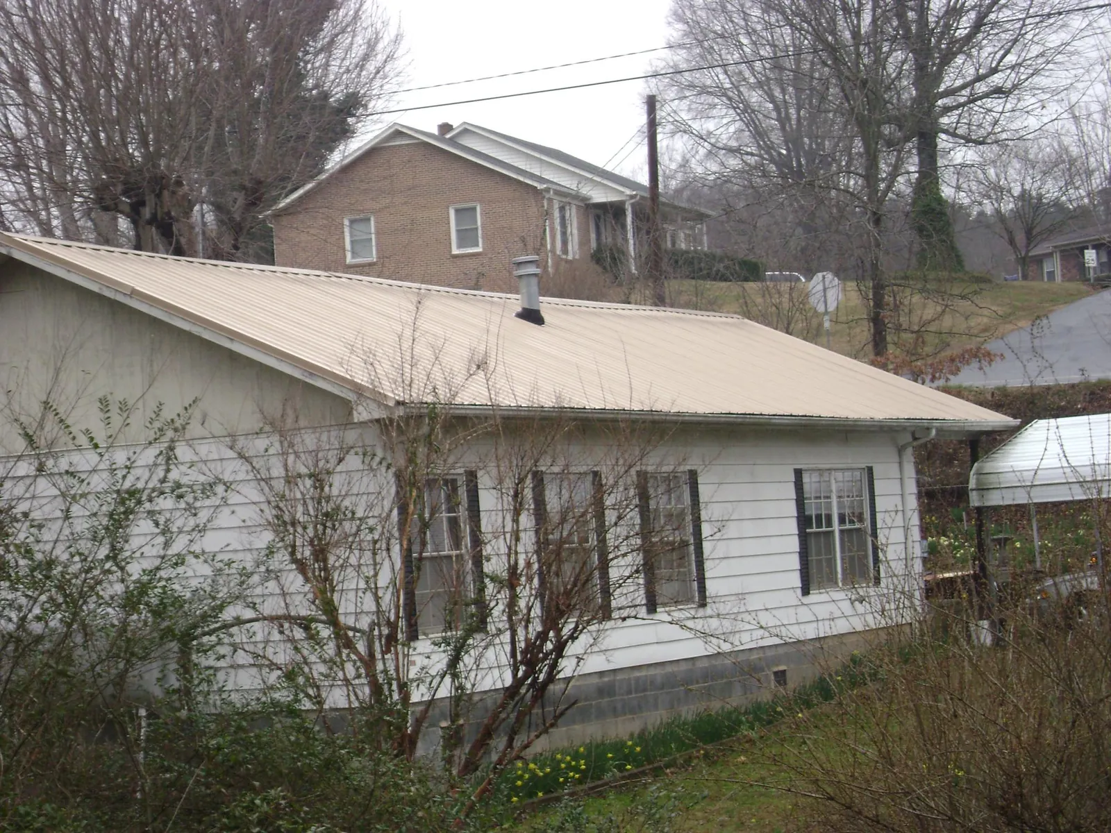 Tan metal roof on a white sided house set into a hillside — Commercial Roofing by Roofing Brothers in Waterford